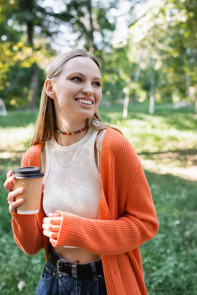 sonriente mujer sosteniendo taza de papel con café para ir en el parque verde - Foto, Imagen