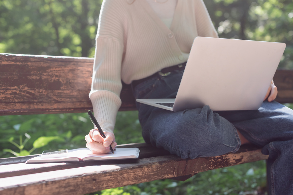 cropped view of woman using laptop while writing in notebook  - Foto, Bild
