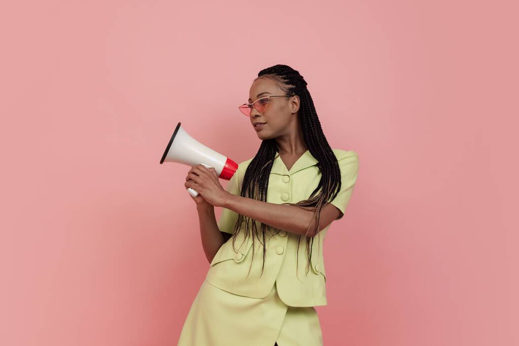 Gelukkig Afrikaans meisje draagt retro stijl outfit met megafoon geïsoleerd op roze achtergrond. Concept van emoties, schoonheid, kunst, mode, jeugd, stijl - Foto, afbeelding