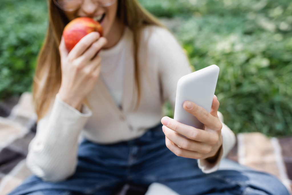 vista ritagliata di donna offuscata mordere mela e scattare selfie su smartphone  - Foto, immagini