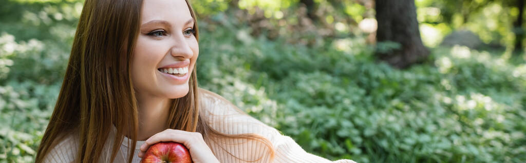 cheerful woman holding red tasty apple in green park, banner - Foto, Imagem