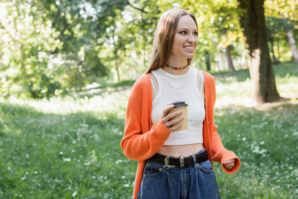 cheerful woman in orange cardigan holding takeaway drink in paper cup - Photo, Image