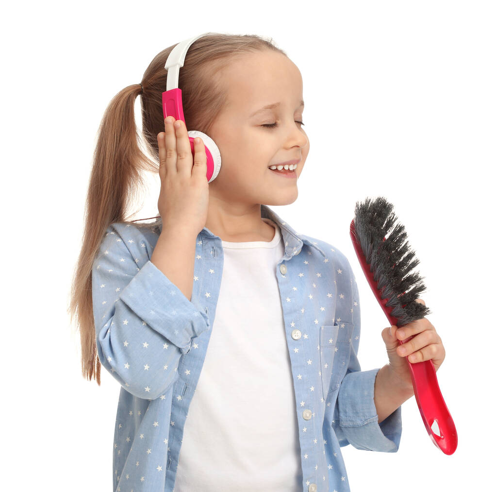 Cute little girl in headphones with brush singing on white background - Фото, изображение