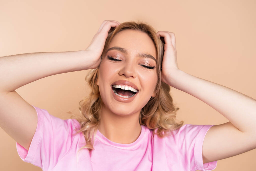 excited woman touching head while laughing with closed eyes isolated on beige - Foto, Imagem