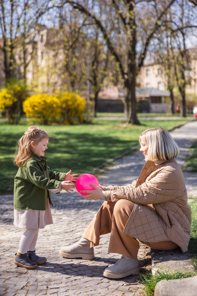 side view of happy mother and daughter playing with ball in city park - Foto, Imagen