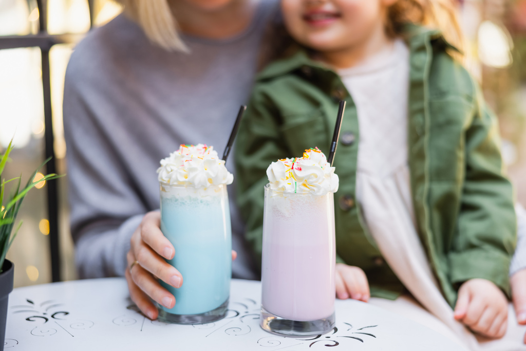 cropped view of blurred mother and daughter near glasses with milkshake and whipped cream - Foto, imagen