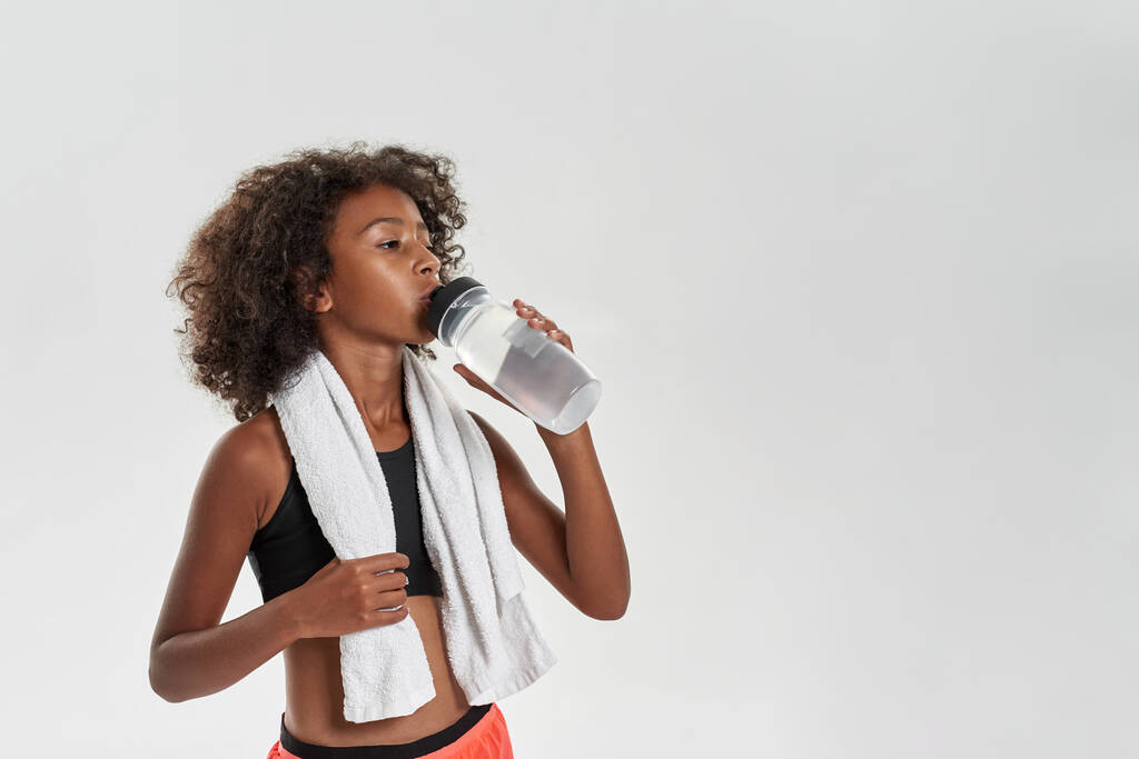 Black girl with towel drinking water from bottle - Foto, Imagen