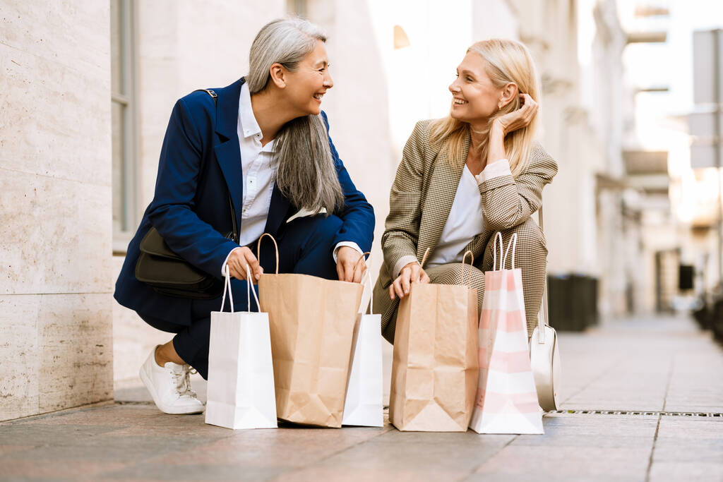 Зрелые многорасовые женщины разговаривают и смотрят в сумки на улице - Фото, изображение