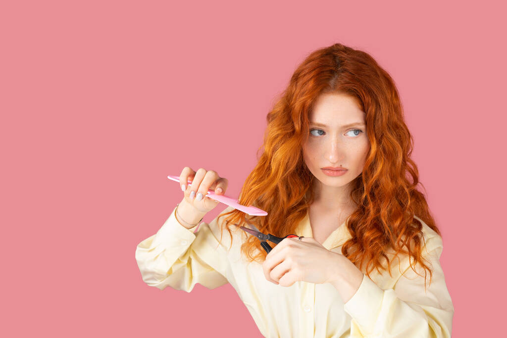 Retrato de una hermosa joven con cabello rojo y expresión facial alterada sosteniendo tijeras y peine en sus manos. - Foto, Imagen