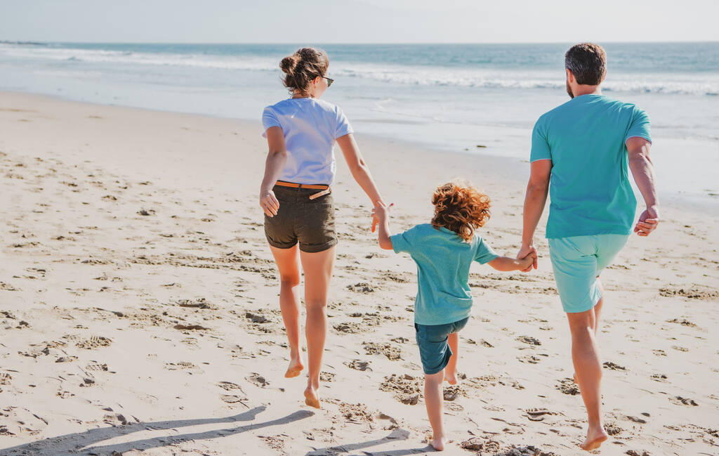 Genç ve mutlu bir ailenin kumsalda yürüyüşünün arka görüntüsü. Ailesi el ele tutuşan bir çocuk. Tam uzunluktaki cep. - Fotoğraf, Görsel