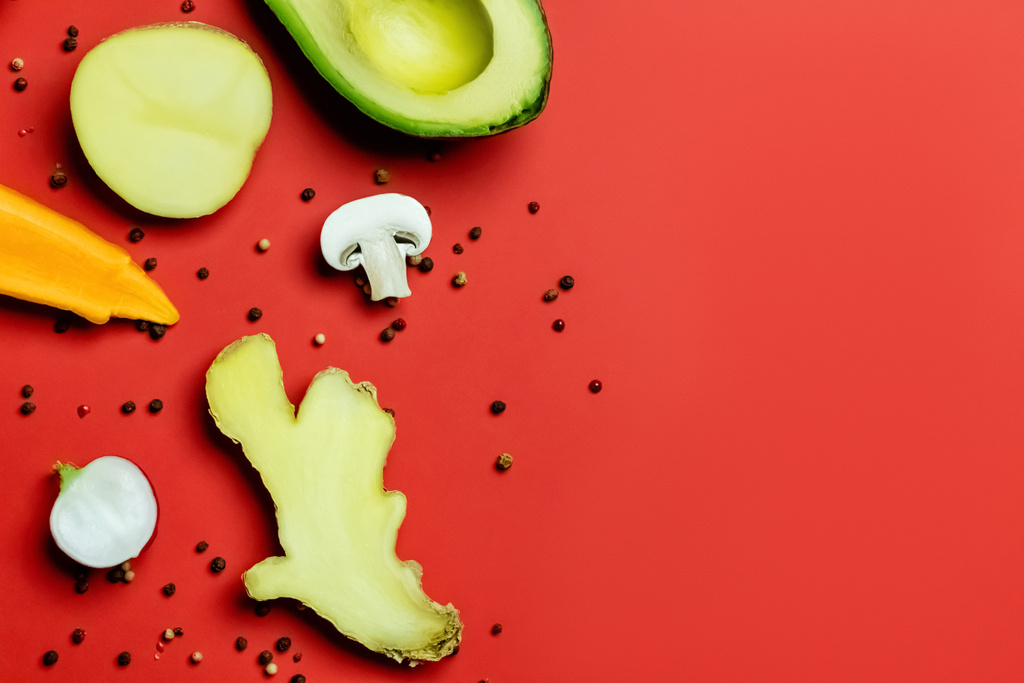 Bovenaanzicht van verse gember, gesneden avocado en peperkorrels op rode achtergrond - Foto, afbeelding