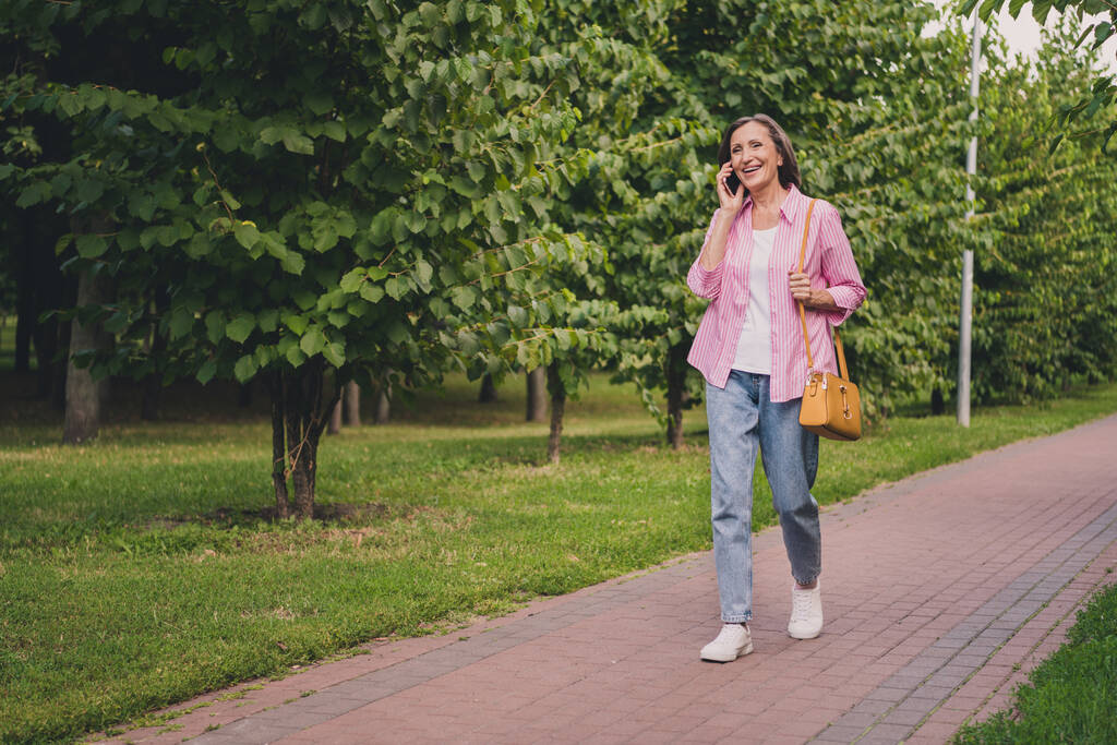 Foto van grappige lieve gepensioneerde vrouw gekleed gestreept shirt praten modern apparaat wandelen buiten landschap - Foto, afbeelding