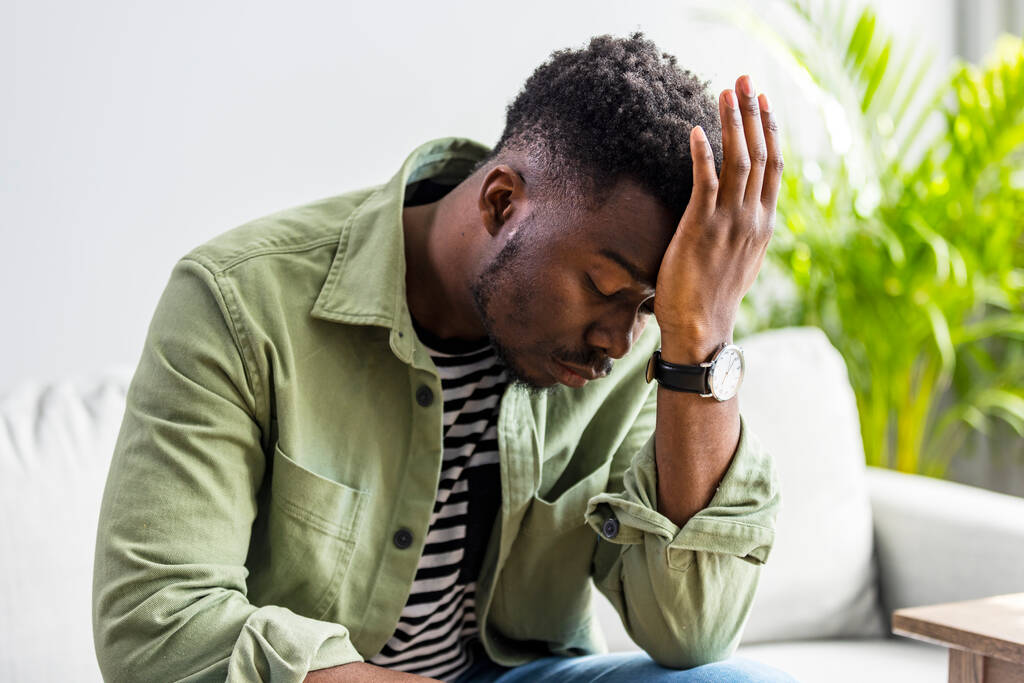 Close-up van de jonge Afro-Amerikaanse man die thuis hoofdpijn heeft, zijn slapen aanraakt, kopieert ruimte, wazige achtergrond. Migraine, hoofdpijn, stress, spanning probleem, kater concept - Foto, afbeelding