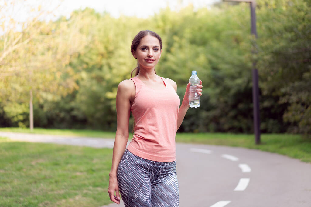 Спортивная женщина, стоящая беговая дорожка в летнем парке с бутылкой воды после выполнения упражнений Кавказская женская утренняя тренировка Бег - Фото, изображение