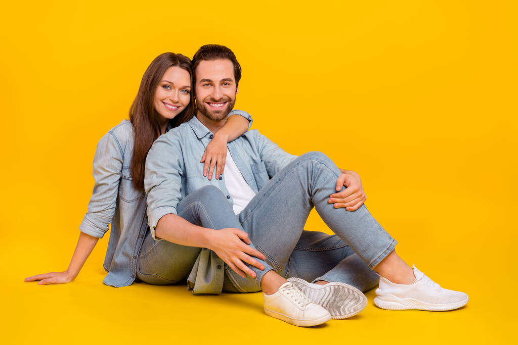 Portrait of two attractive cheerful sweet people sitting hugging spending time isolated over bright yellow color background - Foto, Imagem