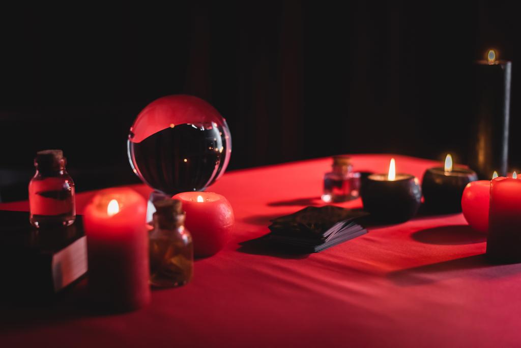Blurred burning candles near magic orb and tarot cards isolated on black  - Photo, Image