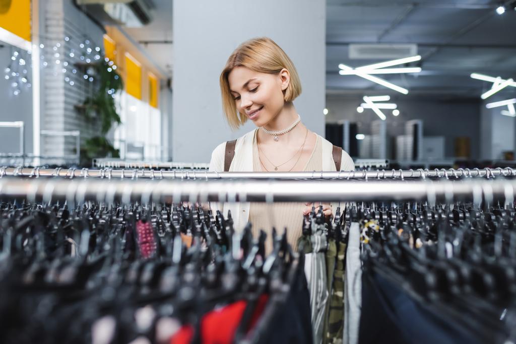 Θετική γυναίκα επιλέγει ρούχα σε ρετρό κατάστημα  - Φωτογραφία, εικόνα