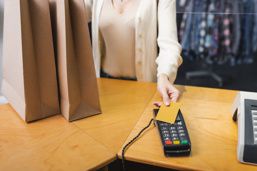 Gewassen weergave van vrouw betalen met creditcard in de buurt van winkeltassen in tweedehands  - Foto, afbeelding