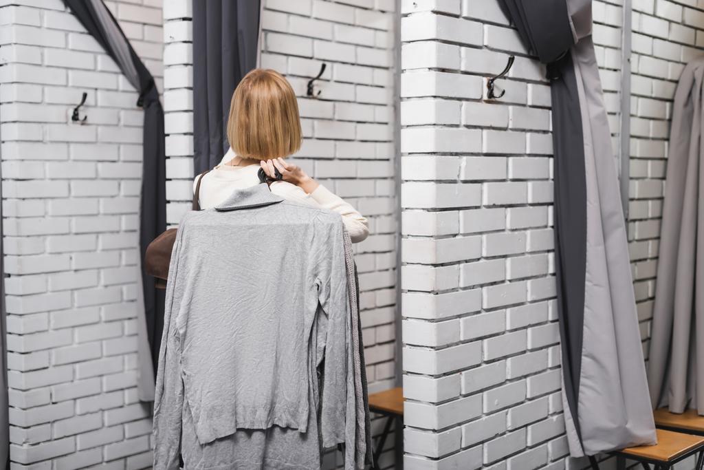 Back view of blonde woman holding hangers with cloth in second hand  - Foto, Imagem