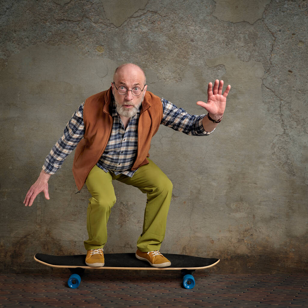 φοβισμένος γενειοφόρος ηλικιωμένος άνδρας ιππασία μακρύ skateboard σε ένα αστικό περιβάλλον grunge - Φωτογραφία, εικόνα