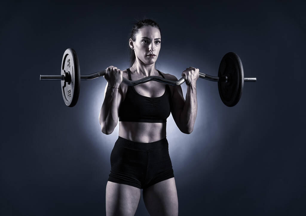 Monochrome toned beeld van een atletische vrouw doet lange halter biceps krullen - Foto, afbeelding