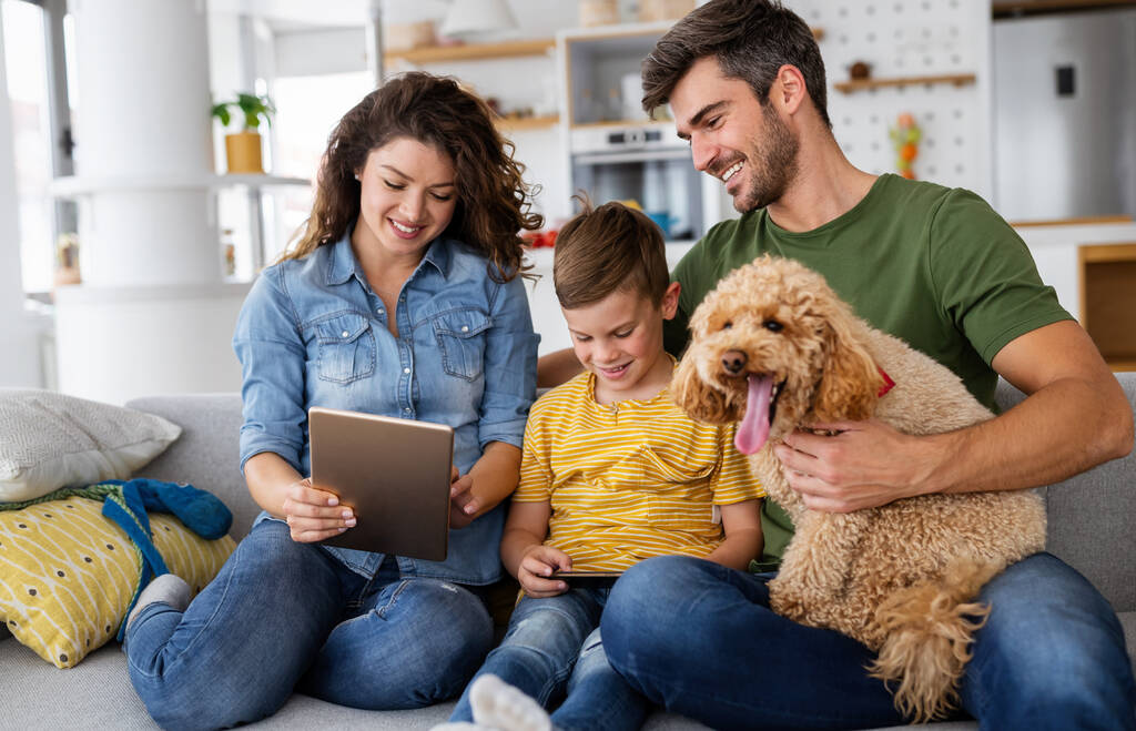 Jovem família feliz com dispositivos modernos e cão se divertindo, jogando em casa - Foto, Imagem