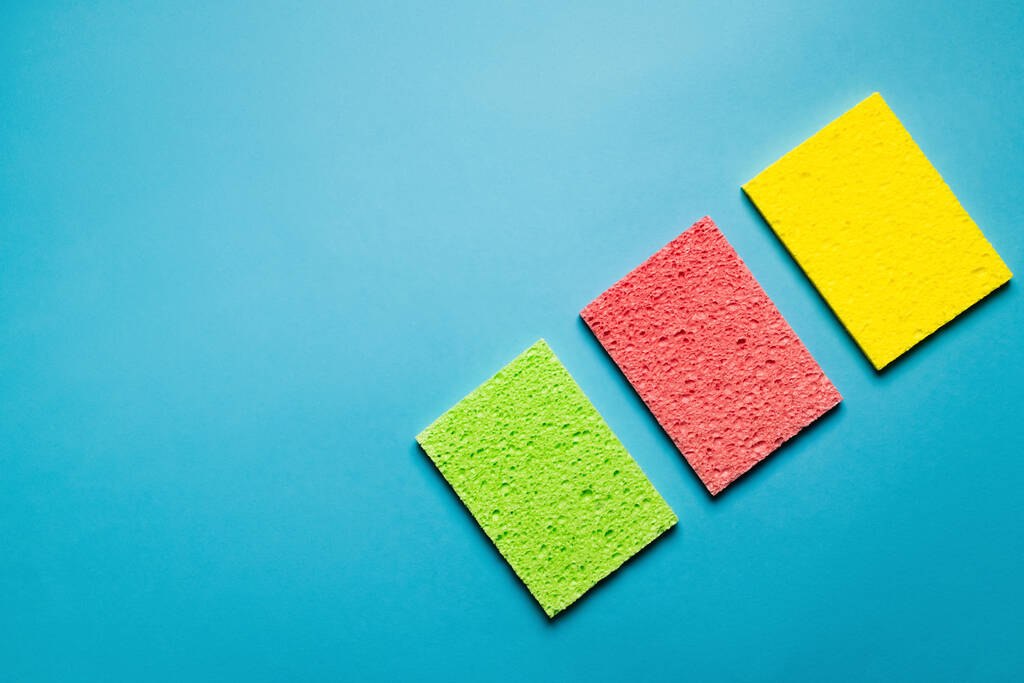 top view of green, pink and yellow absorbent rags on blue background - 写真・画像