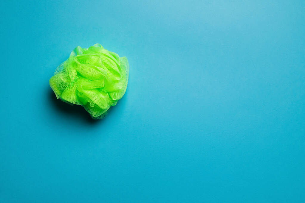 top view of bright green exfoliating mesh body puff on blue background - Foto, afbeelding
