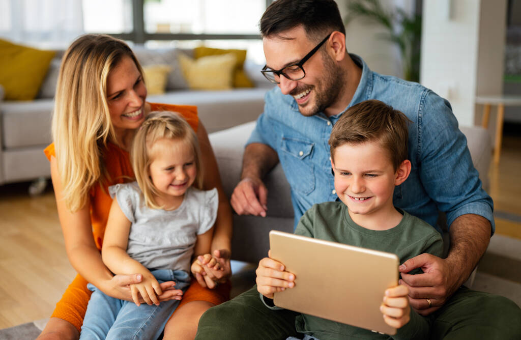 Szczęśliwa młoda rodzina bawiąca się w domu. Rodzice z dziećmi korzystający z urządzenia cyfrowego. Edukacja rodzicielska koncepcja szczęścia. - Zdjęcie, obraz