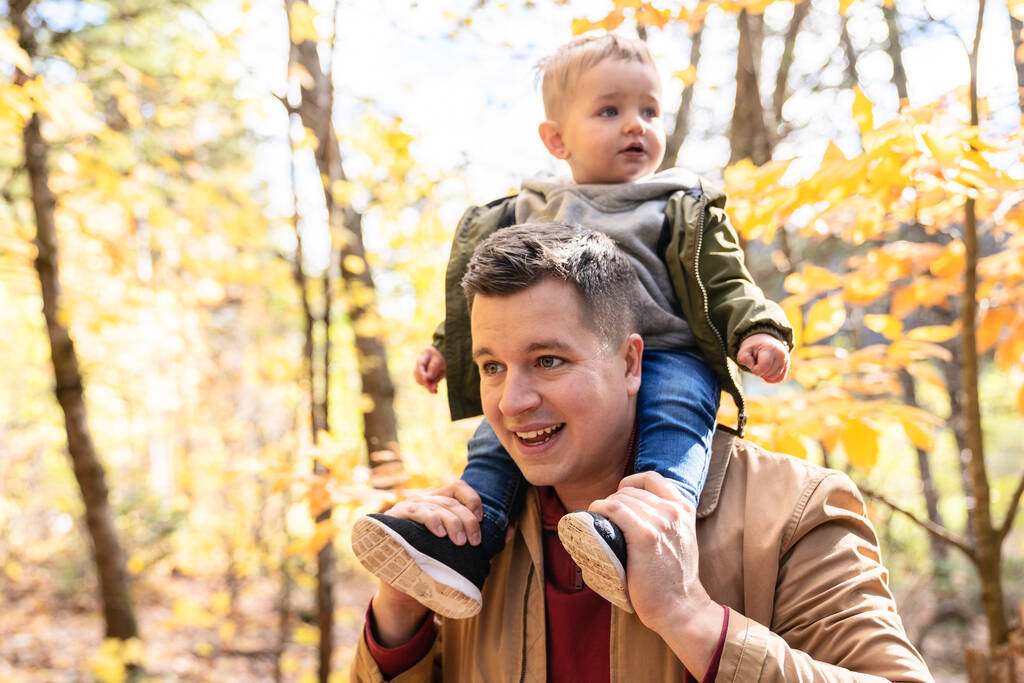 син і її батько в осінній сезон в парку тримають дитину на плечі
 - Фото, зображення