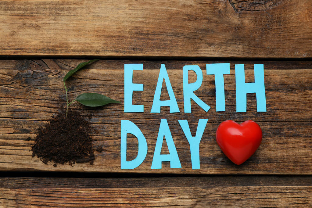 Words Earth Day, soil with plant and decorative heart on wooden table, flat lay - Foto, Bild