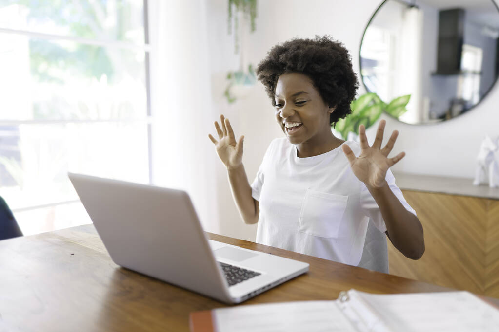 Mosolygós fiatal afrikai női vállalkozó dolgozik online egy laptop, miközben ül a konyhaasztalnál otthon - Fotó, kép