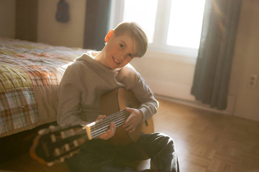 Веселый белый мальчик, играющий на гитаре в своей спальне - Фото, изображение