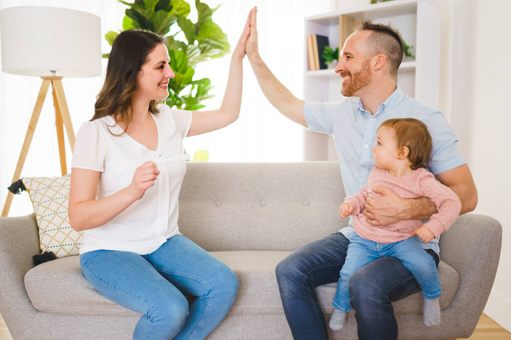 famille heureux avec test de grossesse avec sa femme excitée assis sur un canapé à la maison. - Photo, image