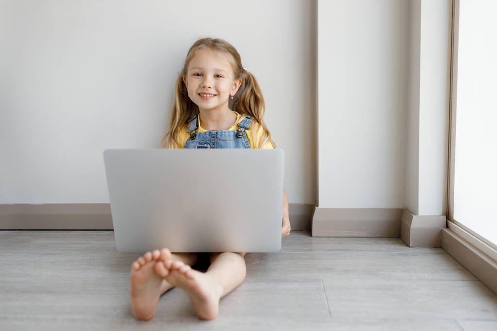 Evde dizüstü bilgisayarı olan sevimli küçük bir kız. - Fotoğraf, Görsel