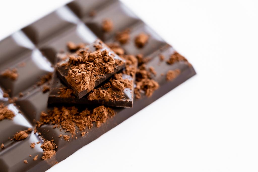 Nahaufnahme von Kakaopulver auf verschwommener Schokolade auf weißem Hintergrund mit Kopierraum  - Foto, Bild