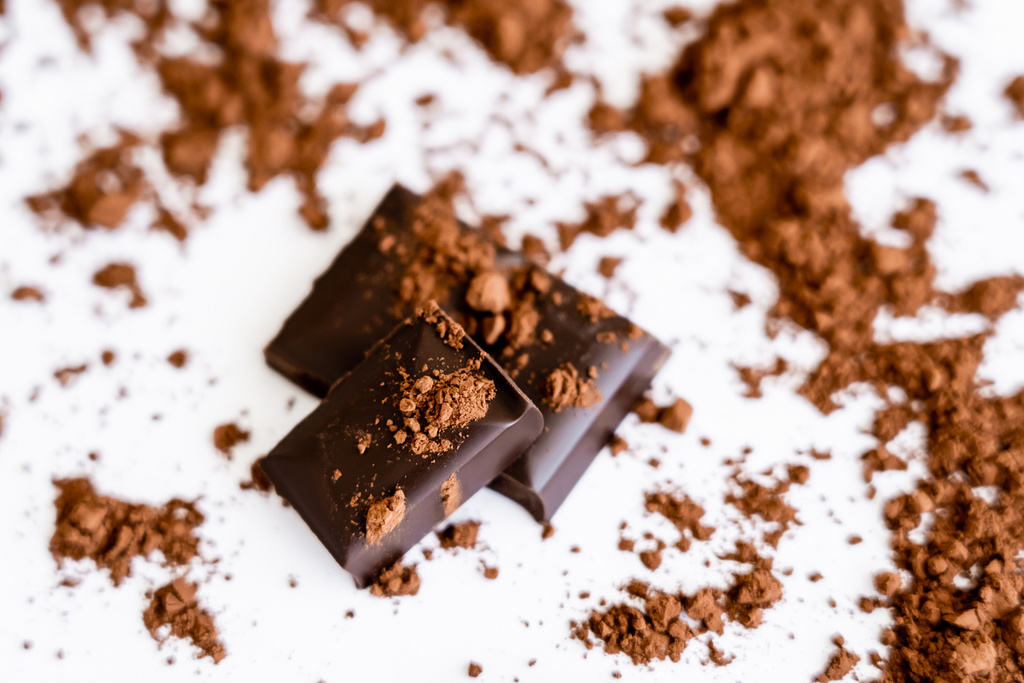 Vista de cerca de piezas de chocolate con cacao seco sobre fondo blanco  - Foto, Imagen
