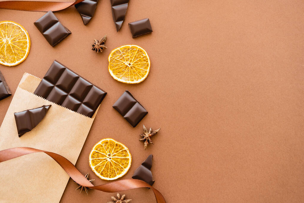 Вид сверху шоколада в ремесленной упаковке, апельсиновые слайсы и анис на коричневом фоне  - Фото, изображение