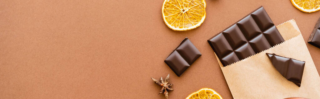 Top view of anise, dry orange slice and chocolate in craft package on brown background, banner  - Фото, изображение