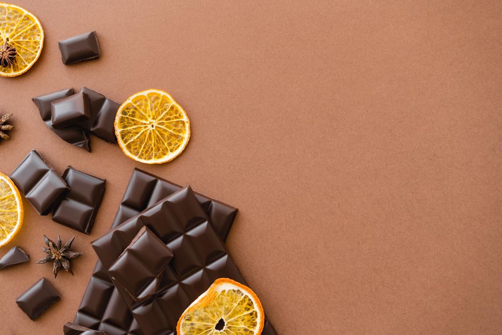 Horní pohled na tmavé čokoládové tyčinky v blízkosti suché oranžové plátky a anýz na hnědém pozadí  - Fotografie, Obrázek