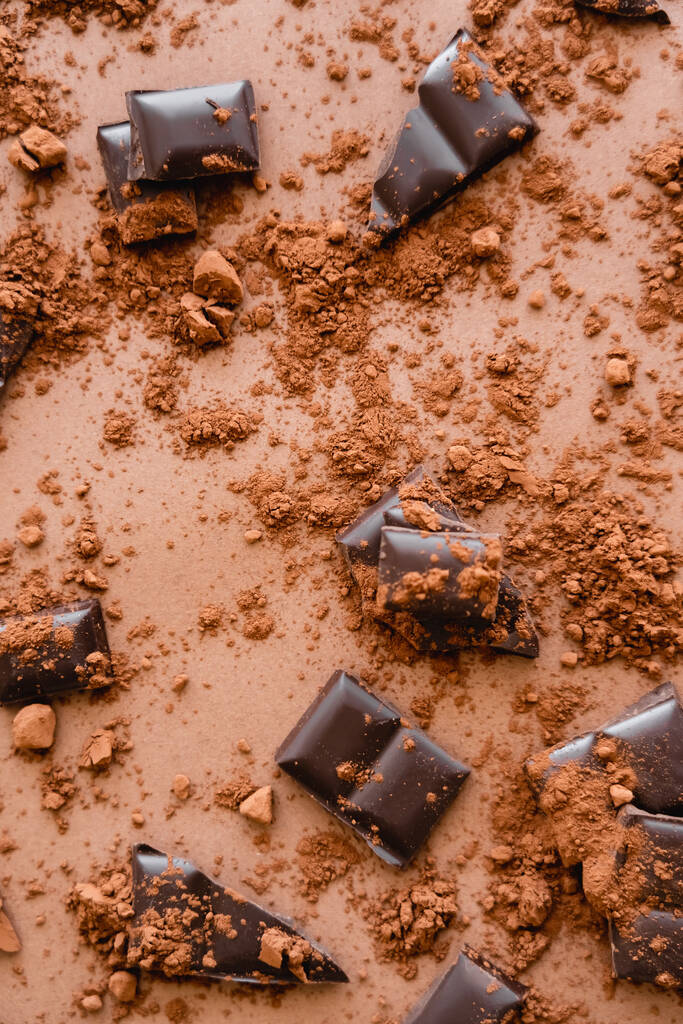 Top view of dry cocoa and dark chocolate pieces on brown background  - Valokuva, kuva