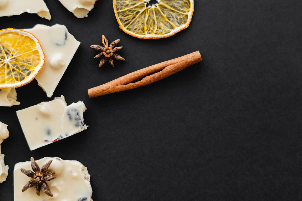 Top näkymä valkoinen suklaa, mausteet ja kuiva oranssi viipaleet mustalla pohjalla - Valokuva, kuva