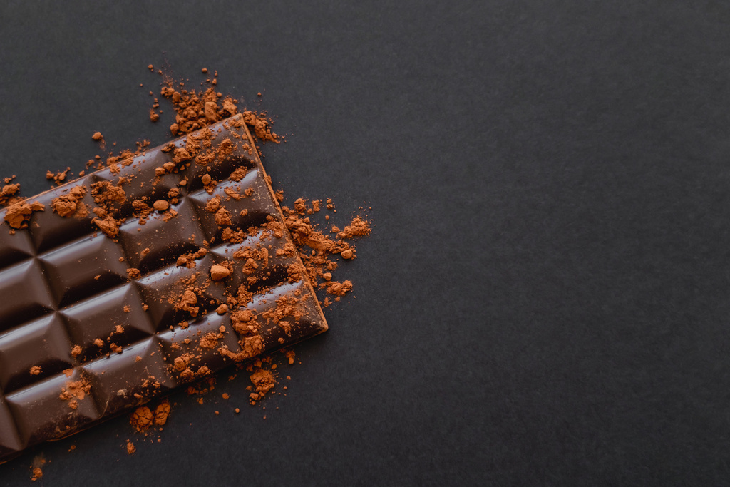 Vista superior de la barra de chocolate negro con cacao en polvo sobre fondo negro con espacio de copia  - Foto, Imagen
