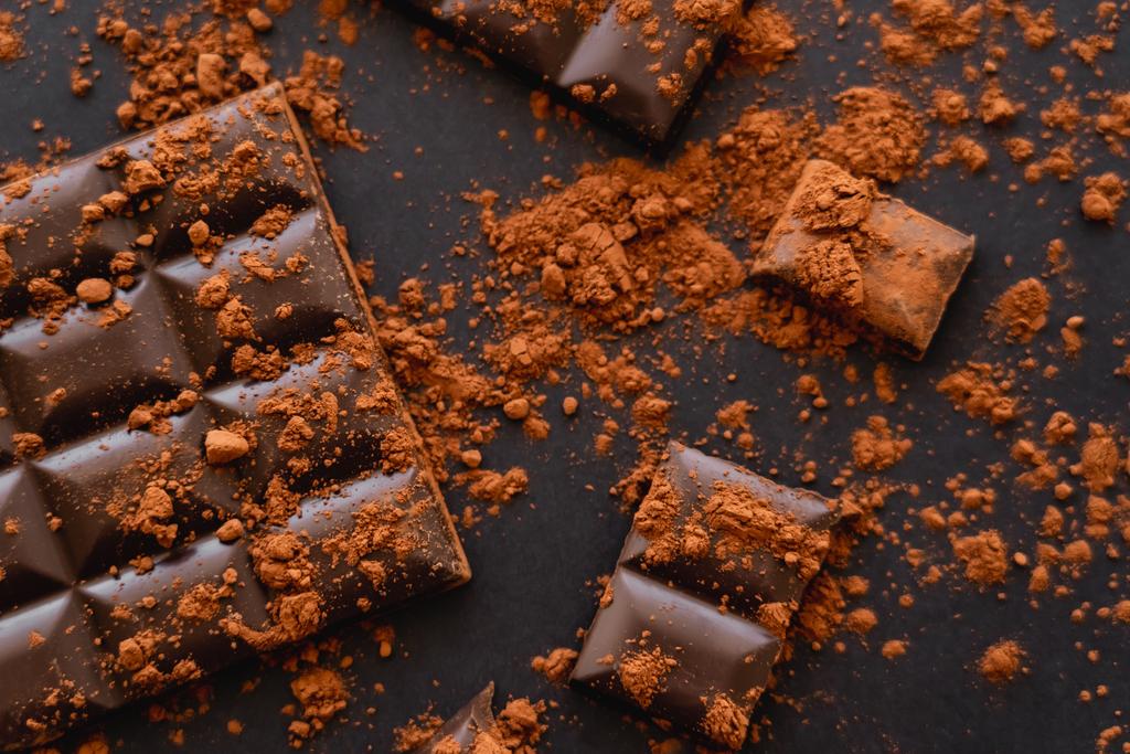 Top view of natural cocoa powder on chocolate on black surface  - Foto, Bild