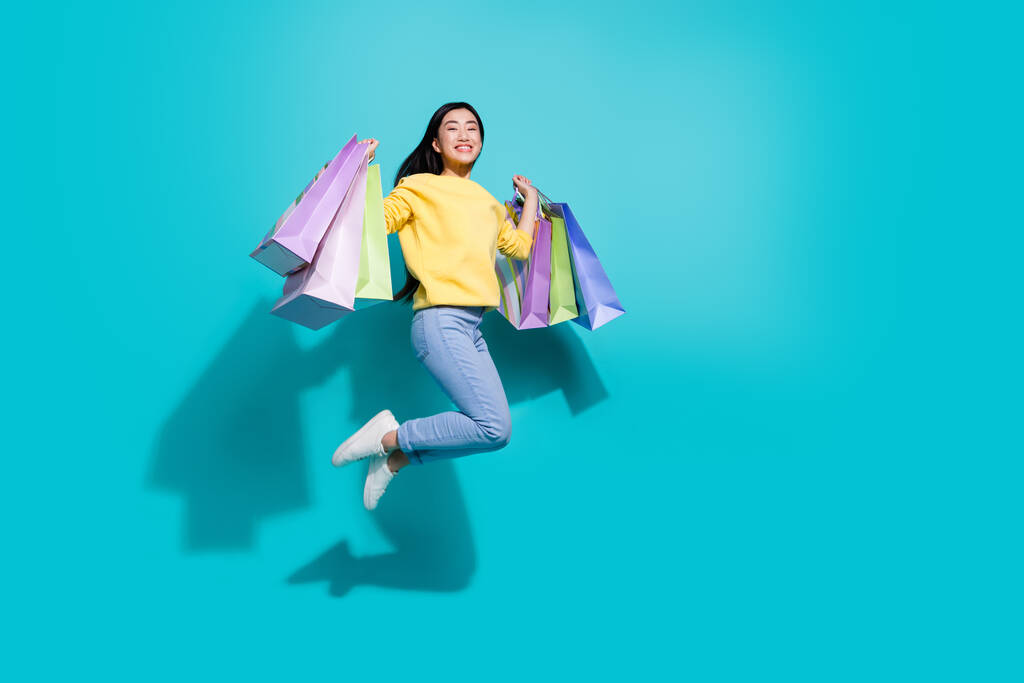 Volledige lengte foto van zoete mooie dame gekleed gele trui springen stijgende shoppers lege ruimte geïsoleerde turquoise kleur achtergrond - Foto, afbeelding