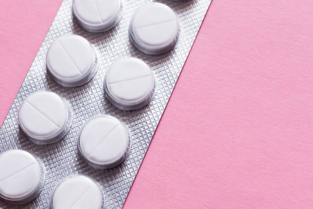 close-up weergave van blisterverpakking met witte ronde vorm pillen geïsoleerd op roze - Foto, afbeelding