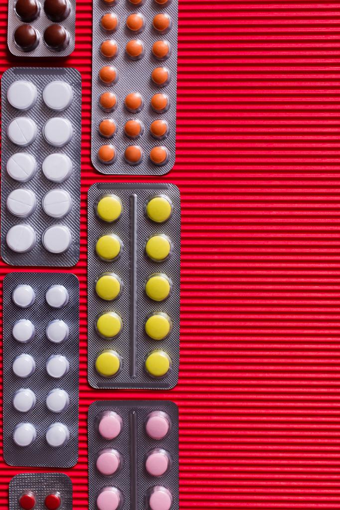 vista dall'alto di blister con diverse pillole su sfondo cremisi testurizzato  - Foto, immagini