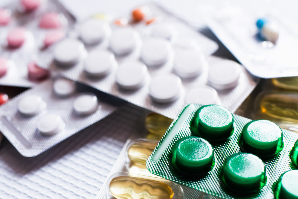 close-up van blisterverpakkingen met verschillende pillen en capsules op getextureerde witte achtergrond - Foto, afbeelding