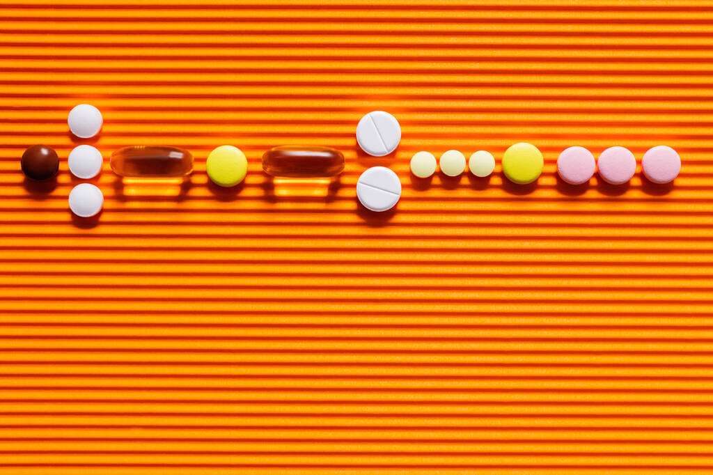 flat lay of different pills on orange textured background - Foto, Imagen