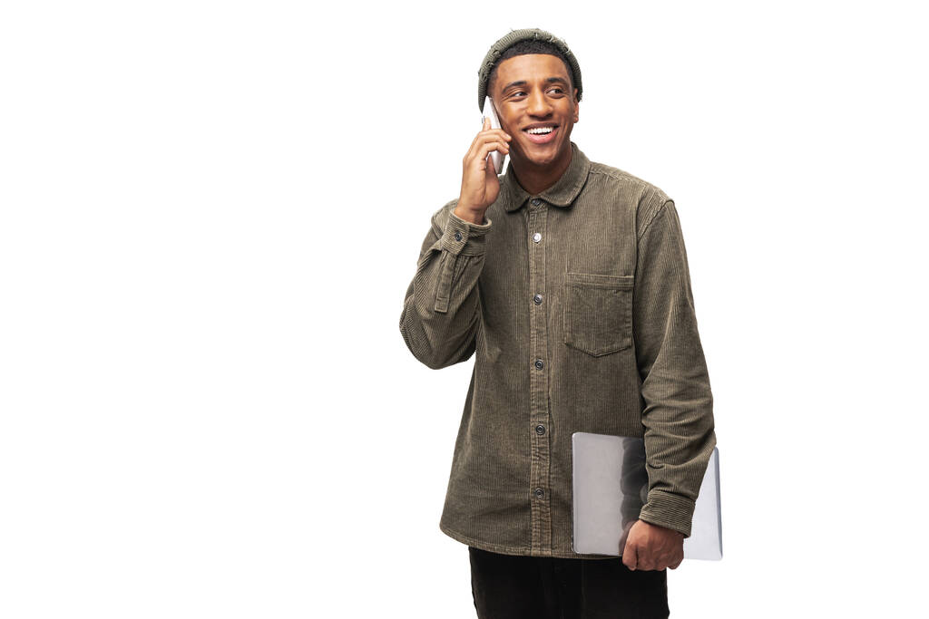 Concept of receiving the good news. Happy hispanic businessman in shirt smiling talking by phone with client after worked with laptop which he holding in the hand - Foto, afbeelding